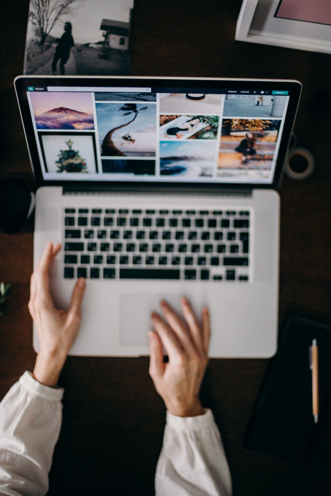Illustrative stock photograph of hands on an open laptop showing a grid of photographs